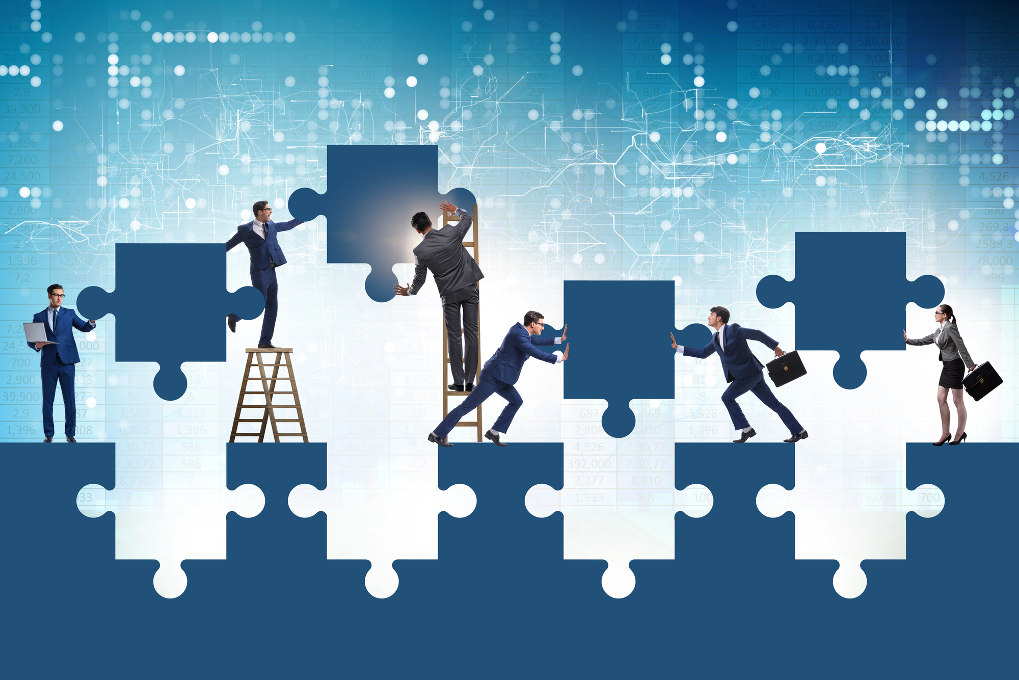 A team of people in suits work together to assemble a larger than life illustrated puzzle.
